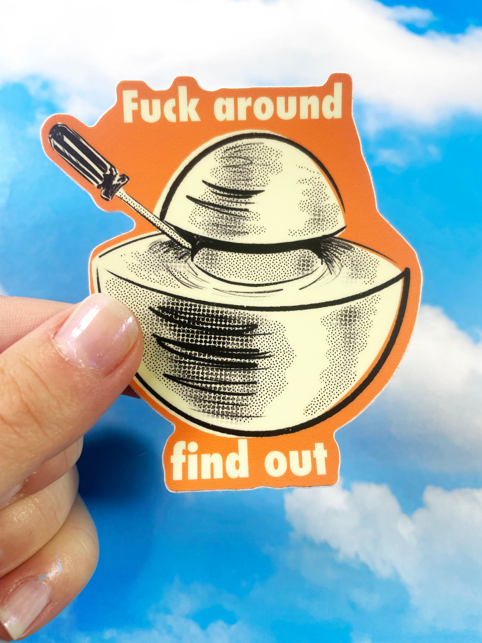 A hand holds up a sticker of an object called the Demon Core. The illustration on the sticker shows the demon core being pried apart with a screwdriver. The font on the sticker says, "Fuck around, Find out".