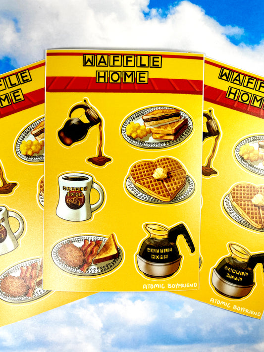 A stack of sticker sheets on a blue cloudy background. The Sticker sheet features artwork of diner-style breakfast foods. There is a syrup carafe, a heart-shaped waffle, a coffee mug and coffee pot, and two plates of toast, eggs, bacon, and hashbrowns.